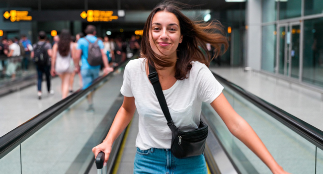 Séjours linguistiques avec LISA! – voyage, aéroport et début de l’aventure Jeune femme avec valise à l’aéroport lors d’un séjour linguistique LISA! enthousiaste pour son arrivée