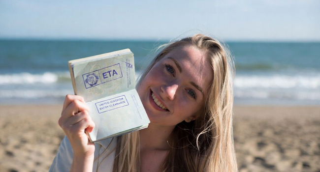 Séjours linguistiques en Angleterre avec LISA! – entrée, visa ETA et préparation Femme sur la plage montrant un passeport avec autorisation ETA lors d’un séjour linguistique LISA! en Angleterre
