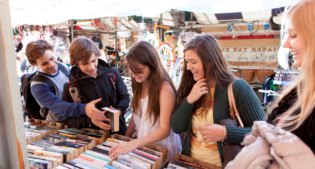 Adultes faisant du shopping sur un marché à Cambridge City Angleterre lors d’un séjour linguistique LISA! découvrent des livres et profitent du temps libre