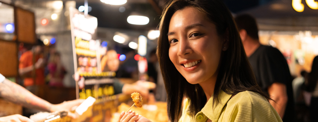 Manger et sortir à Bangkok lors d’un séjour linguistique Une femme asiatique goûte quelque chose à un stand de street food à Bangkok