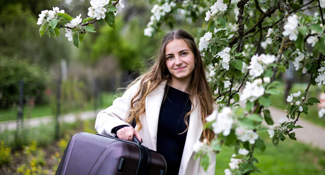 Réservation d’un séjour linguistique LISA! – une jeune fille avec une valise. Une jeune fille avec une valise sous un pommier local symbolise la réservation d’un séjour linguistique LISA!
