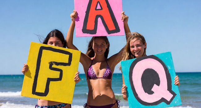 FAQ séjours linguistiques LISA! – réponses aux questions fréquentes Trois étudiantes sur la plage à Bournemouth tiennent des panneaux FAQ lors d’un séjour linguistique LISA!