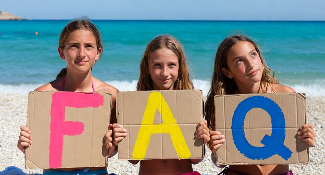 Étudiantes à Jersey tiennent des lettres FAQ sur la plage lors d’un séjour linguistique LISA! avec la mer en arrière-plan