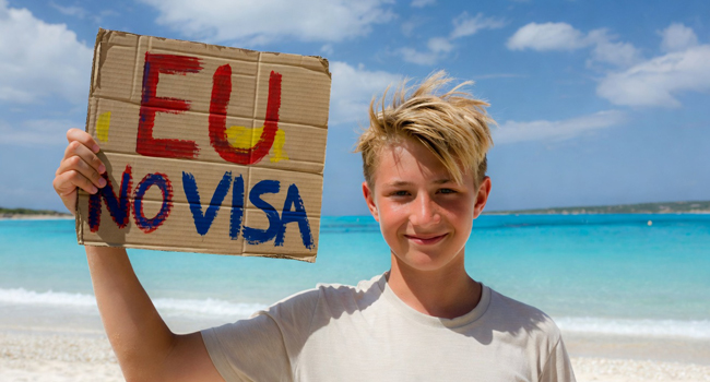 Des étudiants d’un séjour linguistique d’anglais à Malte sur la plage avec un panneau concernant l’entrée sans visa pour les citoyens de l’UE