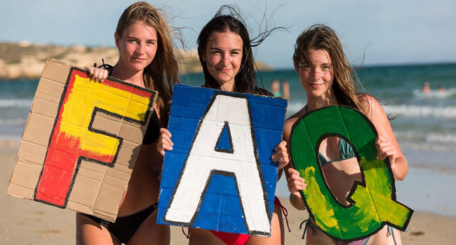 Trois étudiantes sur la plage à Malte tiennent de grandes lettres FAQ lors d’un séjour linguistique LISA! pour étudiants