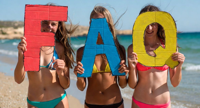 Trois étudiantes d’un séjour linguistique pour étudiants à Malte sur la plage de St. Julian’s avec de grandes lettres FAQ