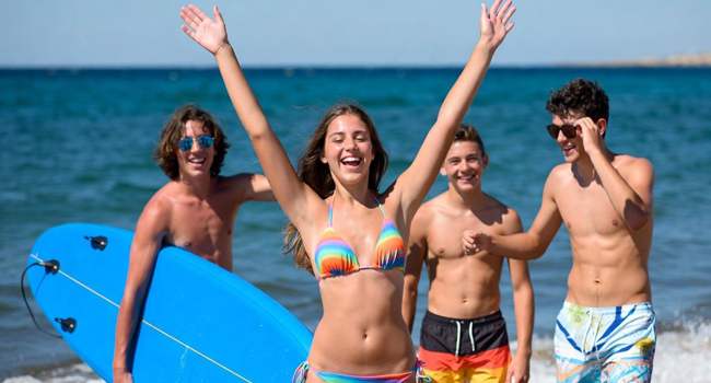 Une fille lève les bras avec trois garçons et la mer en arrière-plan