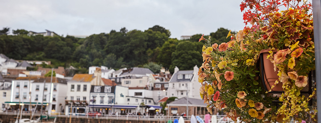 Am Hafen auf der Insel Jersey bei einer Sprachreise Häuserzeile am Meer mit Restaurants, im Vordergrund Blumen