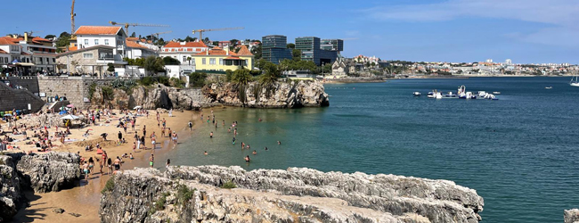 Blick in eine Bucht am Meer vor Lissabon mit vielen badenden Menschen