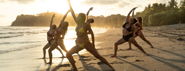 Mehrere Frauen in Bikini machen am Morgen am Strand Yogaübungen
