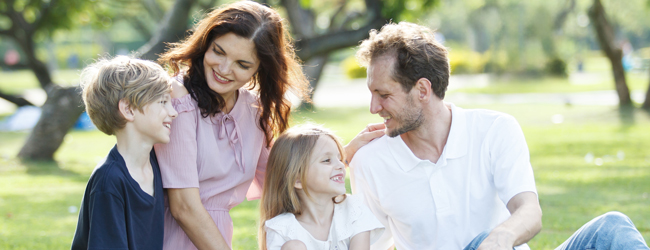 Eine Familie mit zwei Kindern sitzt in einem Park unter schattigen Bäumen bei einer Sprachreise für Familien