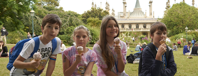Freizeit und Eis essen bei einer LISA! Sprachreise für Familien Vier Kinder sitzen vor dem Royal Pavillion in Brighton im Grünen und essen ein Eis