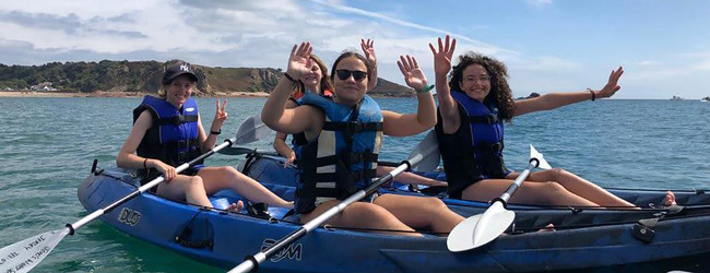 Paddeln auf dem Meer bei einer Schülersprachreise in Jersey Vier Mädchen winken in die Kamera und sitzen in Paddelbooten bei einer Sprachreise in Jersey