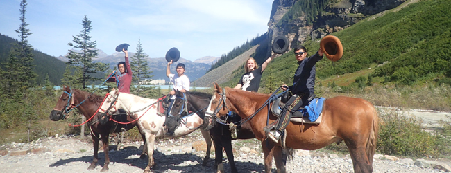 Ausritt in den Rocky Mountains bei einer Schülersprachreise in Calgary Vier Jugendliche sitzen auf Pferden und winken in die Kamera bei einer LISA! Schülersprachreise in Calgary