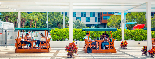 Schüler sitzen in kleinen orangnen Loungebänken mit Dach auf dem Universitätsgelände in Miami