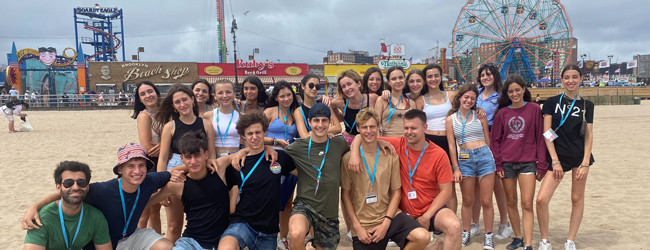 Eine Schülergruppe steht am Strand vor Fahrgeschäften eines Freizeitparks in New York