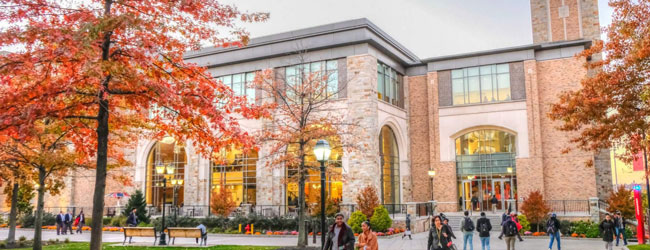 Ein Backsteingebäude mit Bäumen im Herbstlaub und Menschen davor